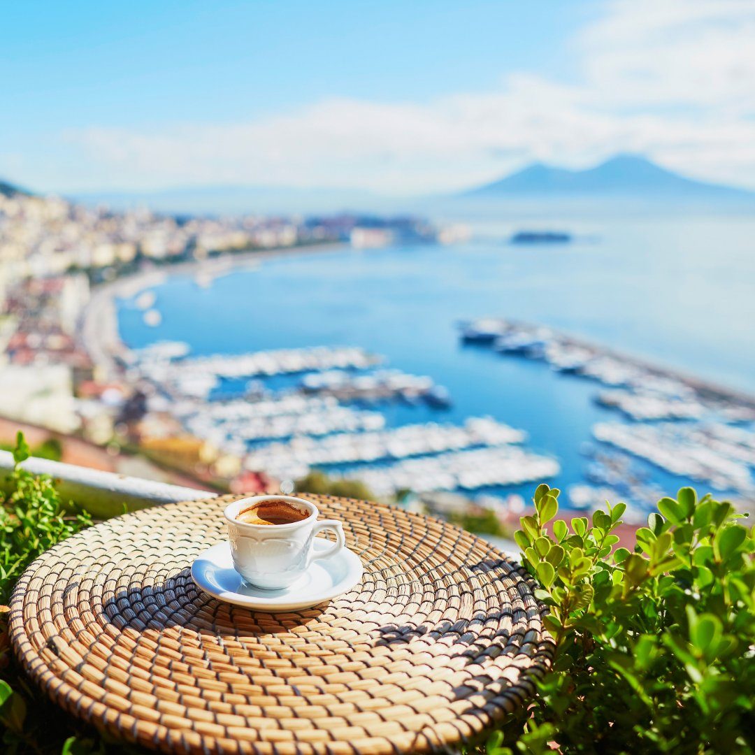 Tazzina di espresso napoletano su un tavolino di vimini affacciato sul Golfo di Napoli e sul Vesuvio
